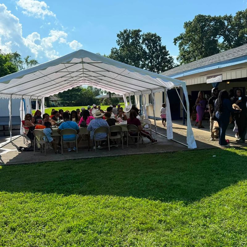 A large gathering eating together under a tent beside the pavilion