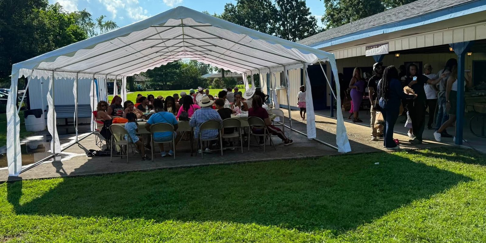 A large group eating under a tent set up beside the pavilion